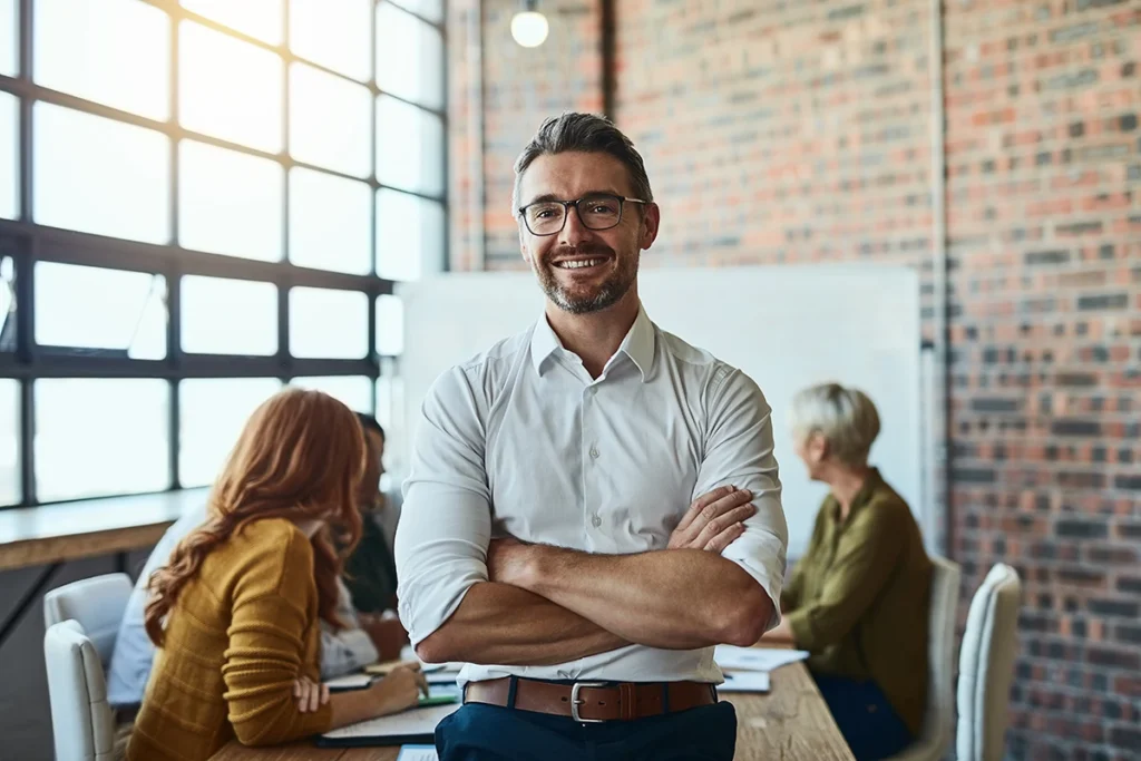 businessman standing in the office with his arms folded looking confident and smiling at the camera